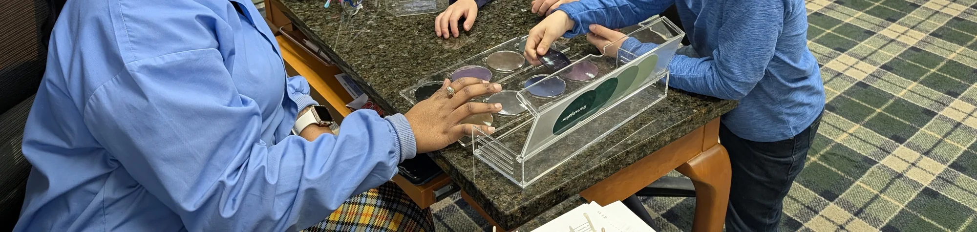 A member of the Evergreen Eye Care team showing a tray of lenses across the front counter.